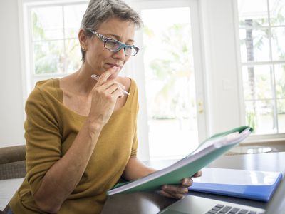 Woman at a laptop holding a folder in a home office 