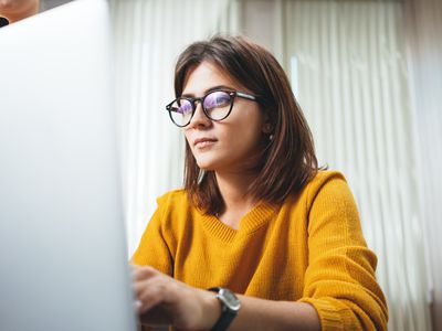 Portrait of pensive business woman wearing glasses at workplace in office. Young handsome female worker using modern laptop