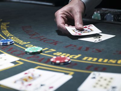 Male croupier holding card at Blackjack table.