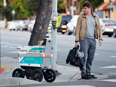 A Serve Robotics autonomous delivery robot crosses onto a sidewalk beside a pedestrian.