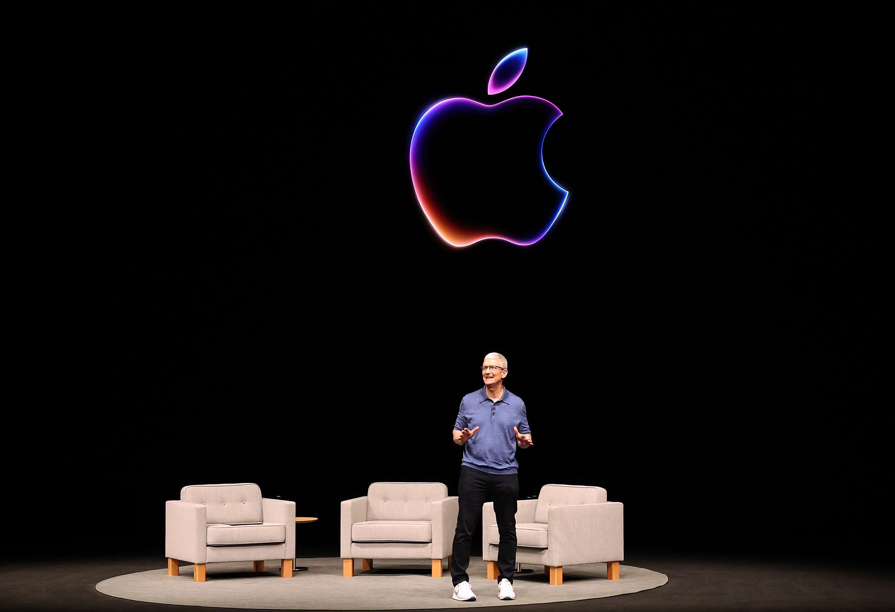 Apple CEO Tim Cook speaks on stage, standing beneath a colorful Apple logo. 