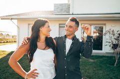 Couple in front of a house, smiling. The man is holding a key.