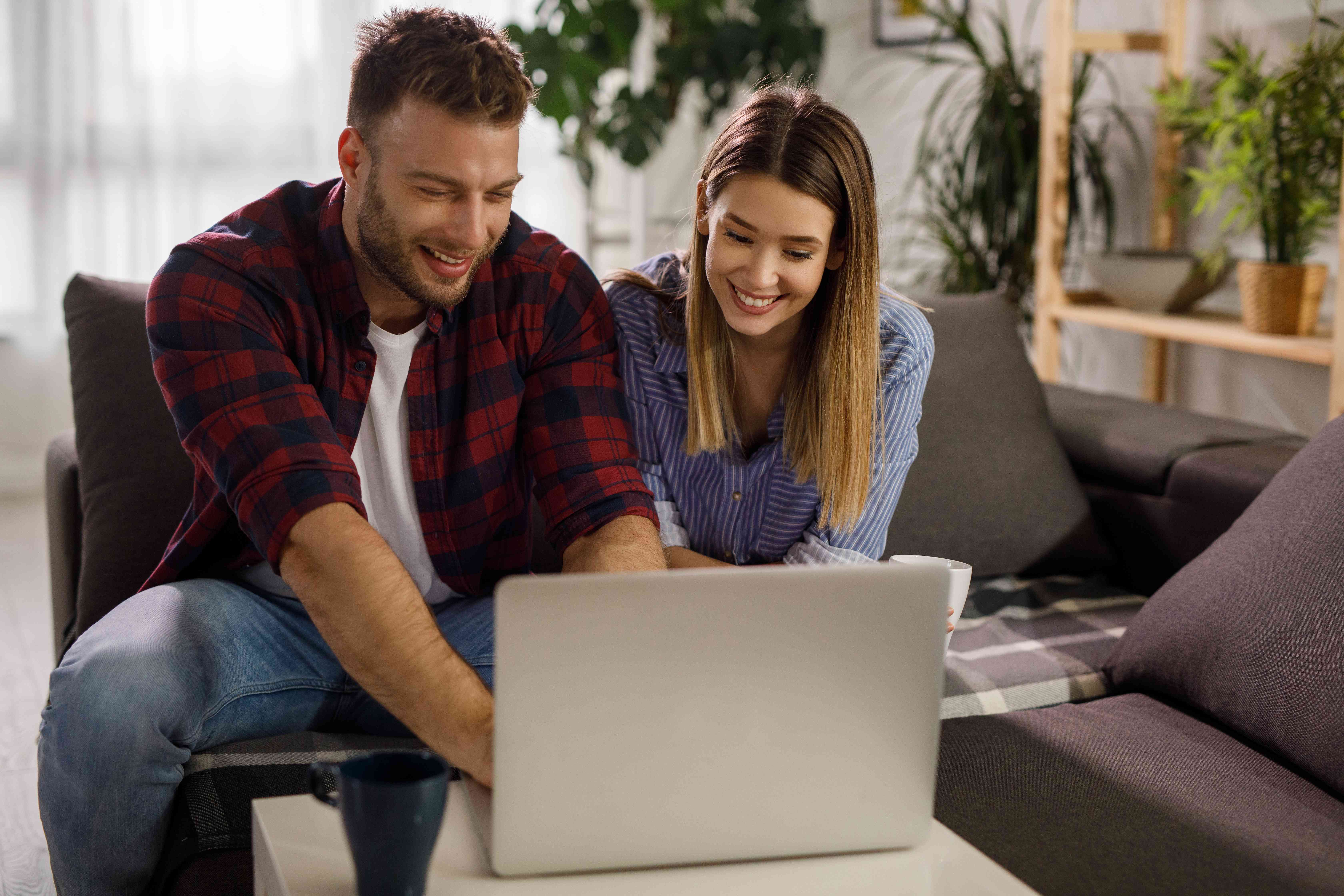 Young couple sitting in their living room and looking happily at a laptop screen