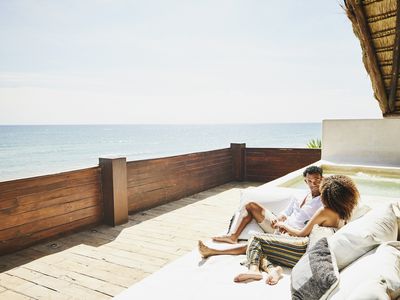 Wide shot of couple relaxing on deck of luxury tropical villa overlooking ocean