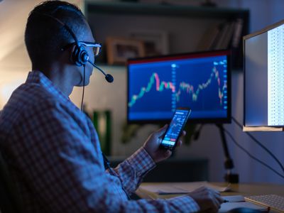 A person looks at a currency trading app on their smart phone from an office.