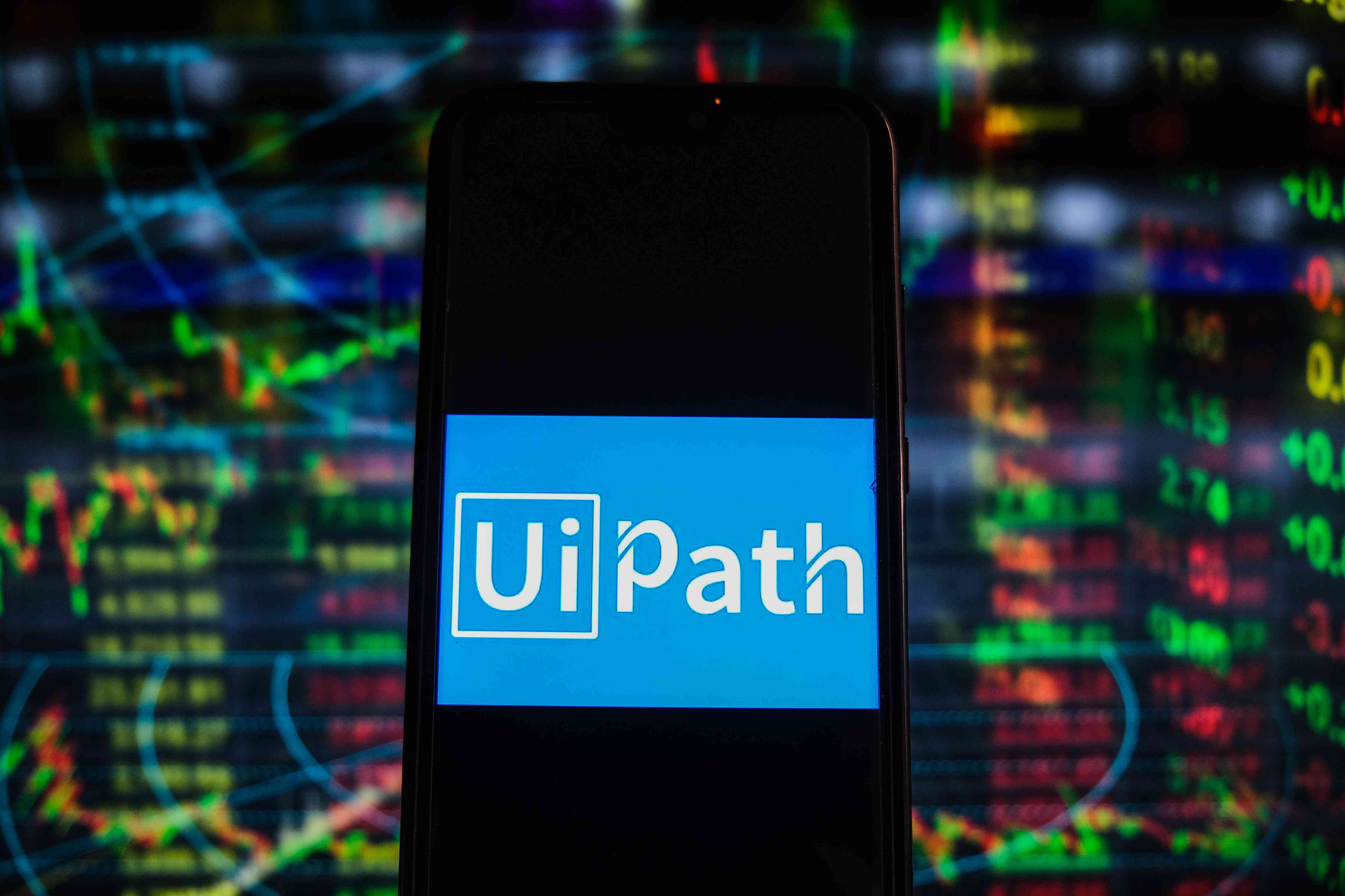 An illustration of the UiPath logo on a mobile device in front of market data. 