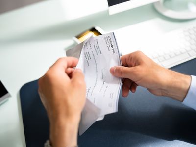 A worker pulls their paycheck out out of an envelope while sitting at their office desk.