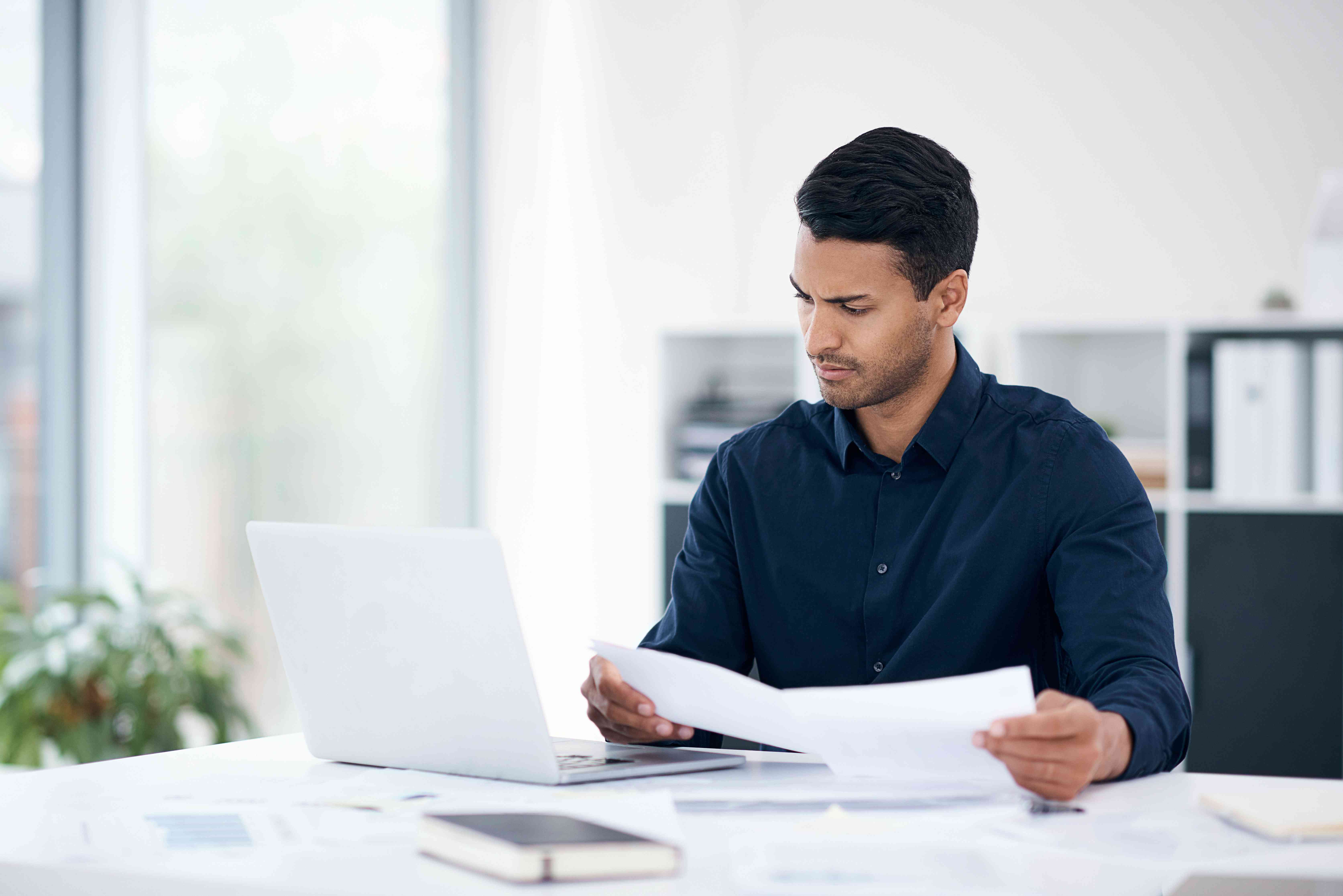 An person sitting in front of a laptop while sorting through paperwork about his tracker mortgage.