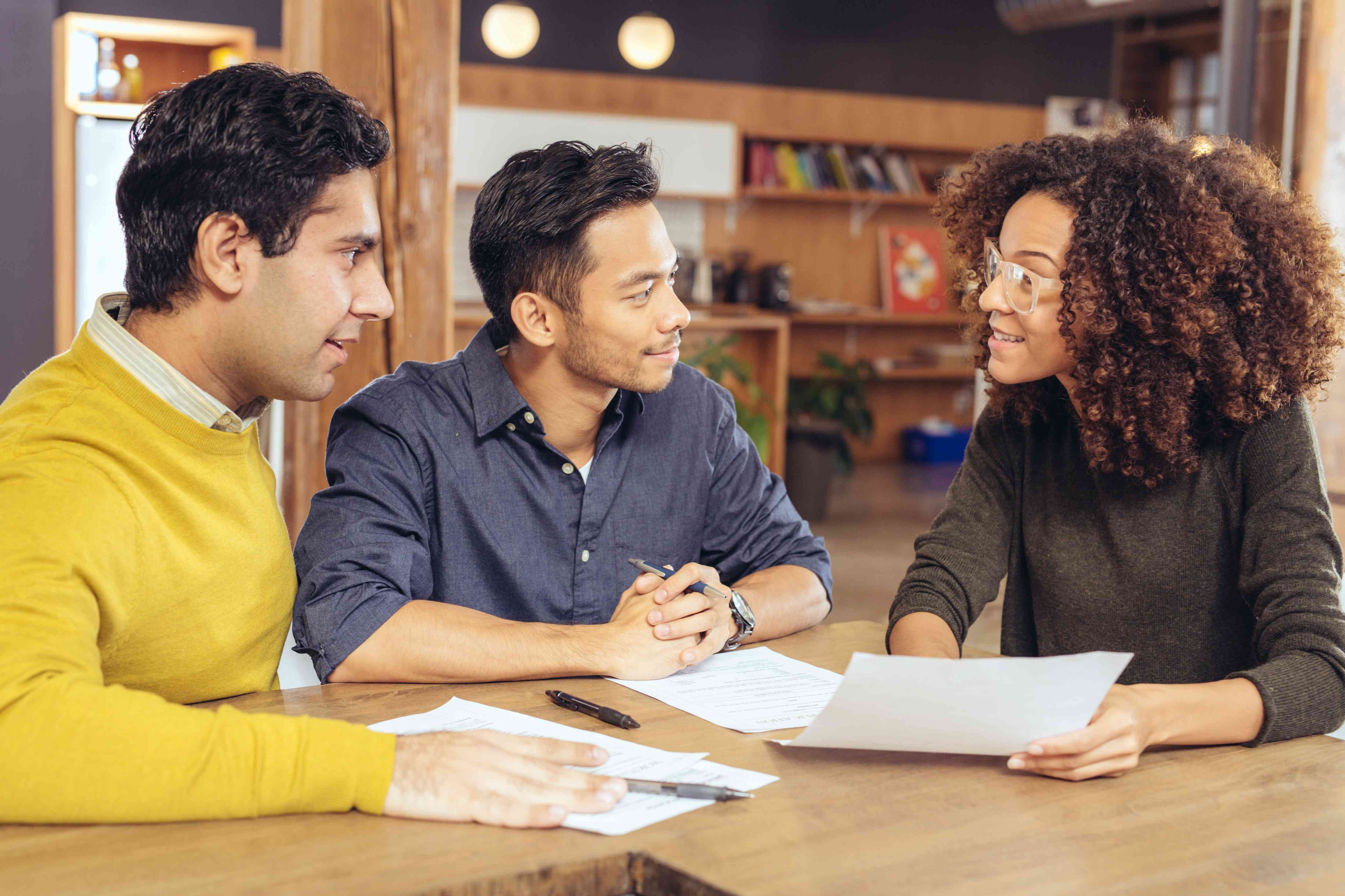  Seated at a table, LGBTQ+ couple goes over paperwork with a financial advisor.