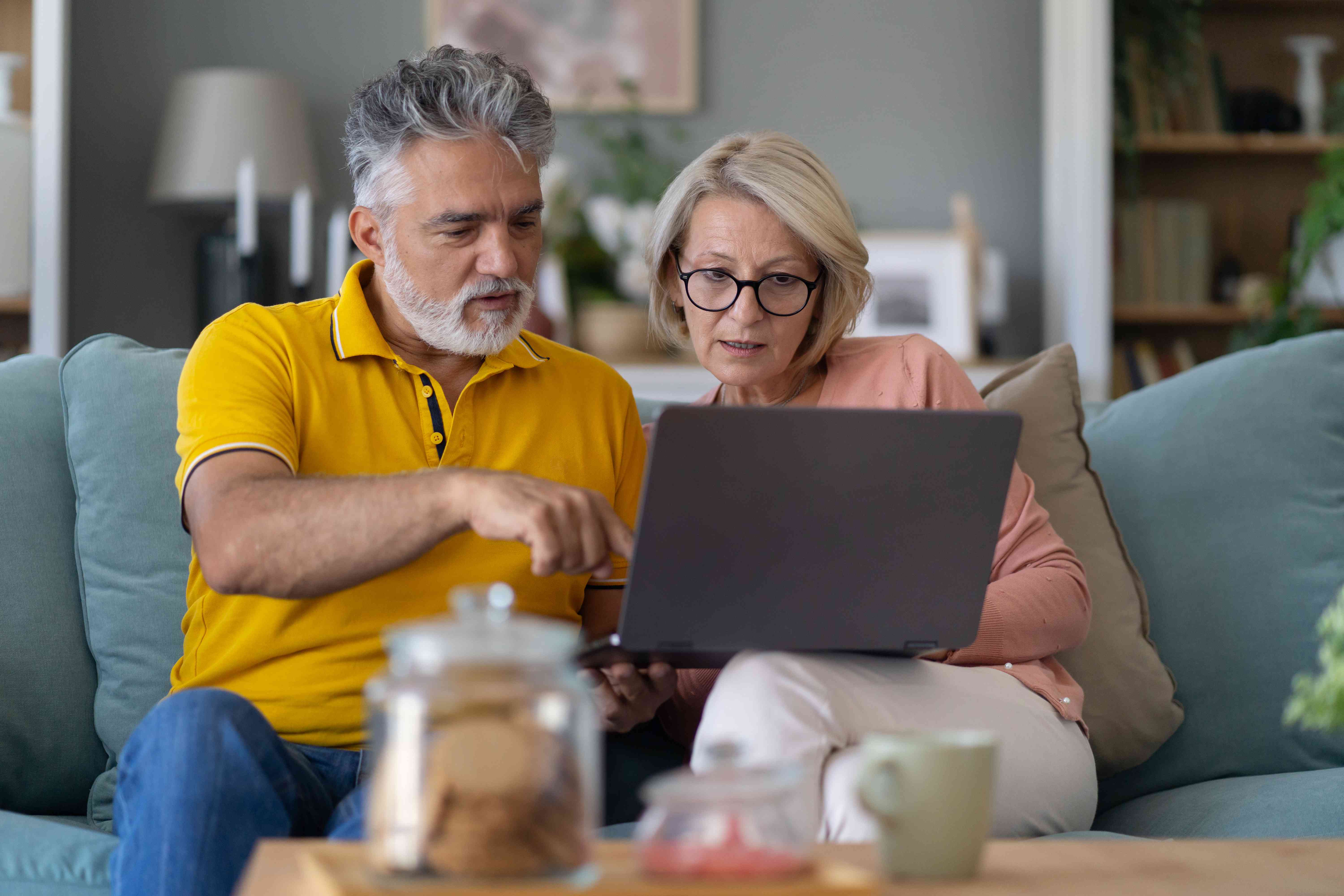 Older couple sitting on their living room couch intently looking together at their laptop