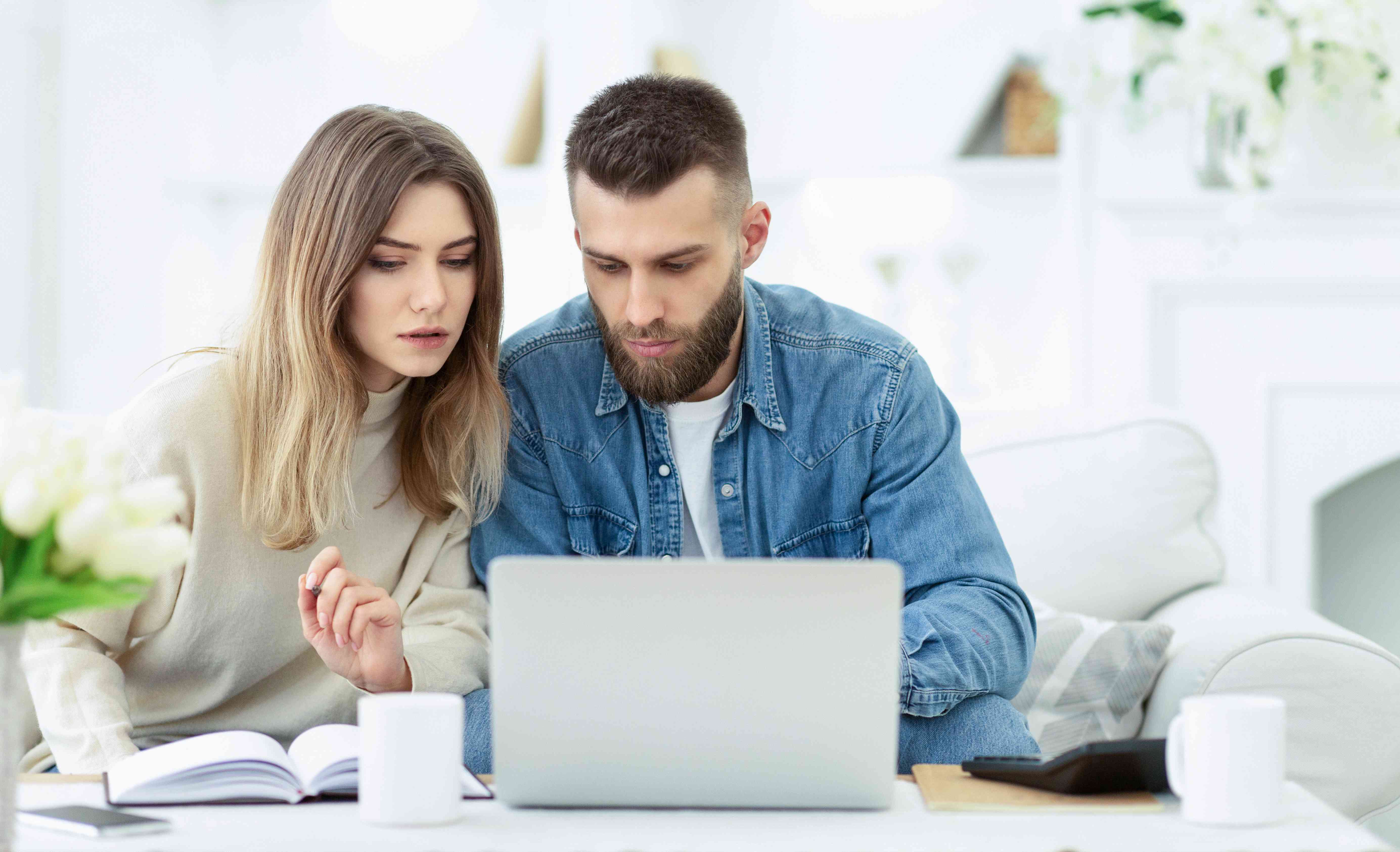 Young couple at home in their living room, looking seriously at a laptop screen together