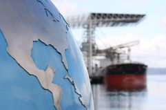 A globe with focus on the United States (USA) and Central America contrasted against a blurred background of a bulk cargo ship.