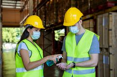 Warehouse worker wearing protective mask and using hand sanitizer