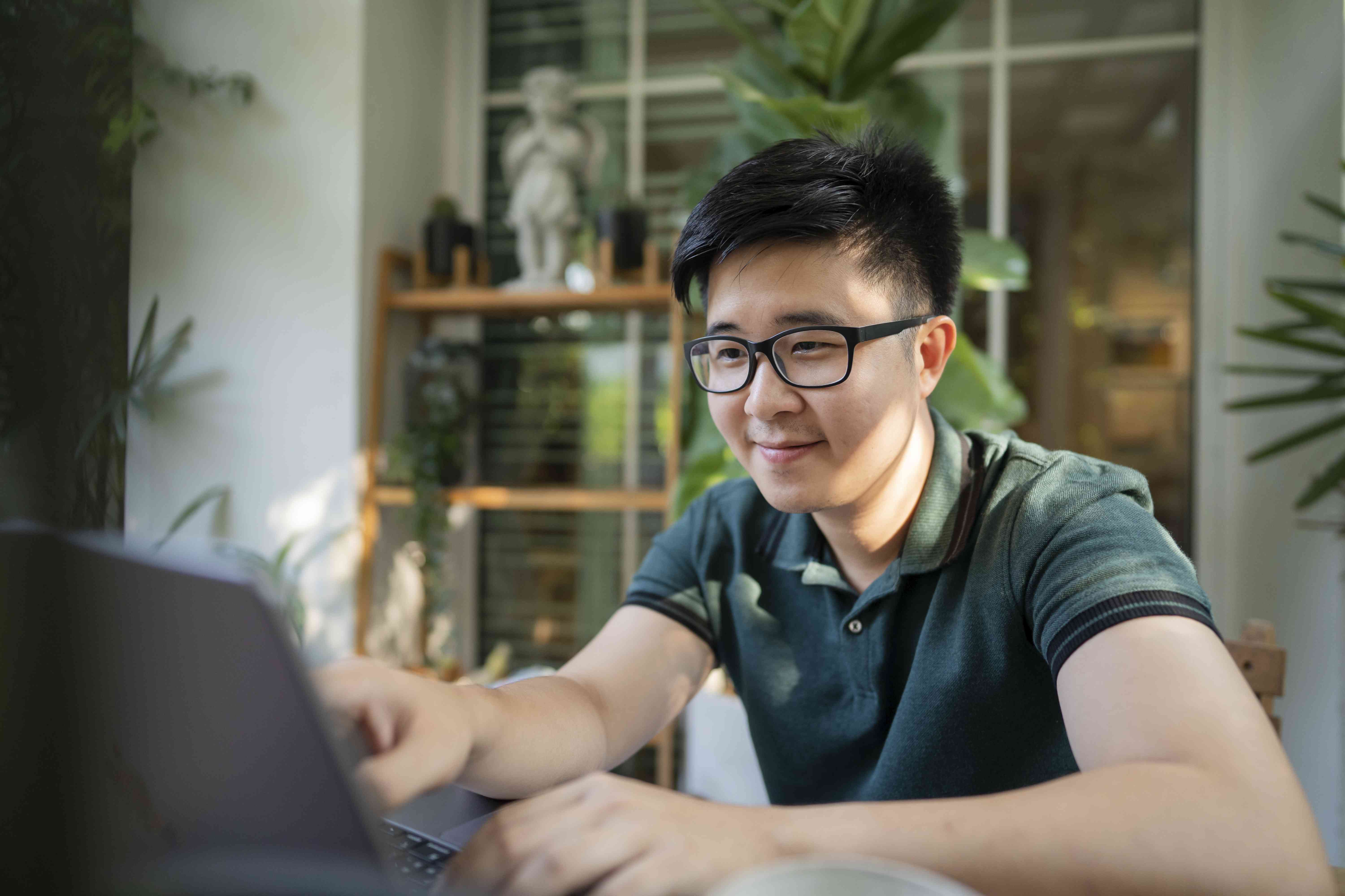 A man with glasses sits at a table with a laptop