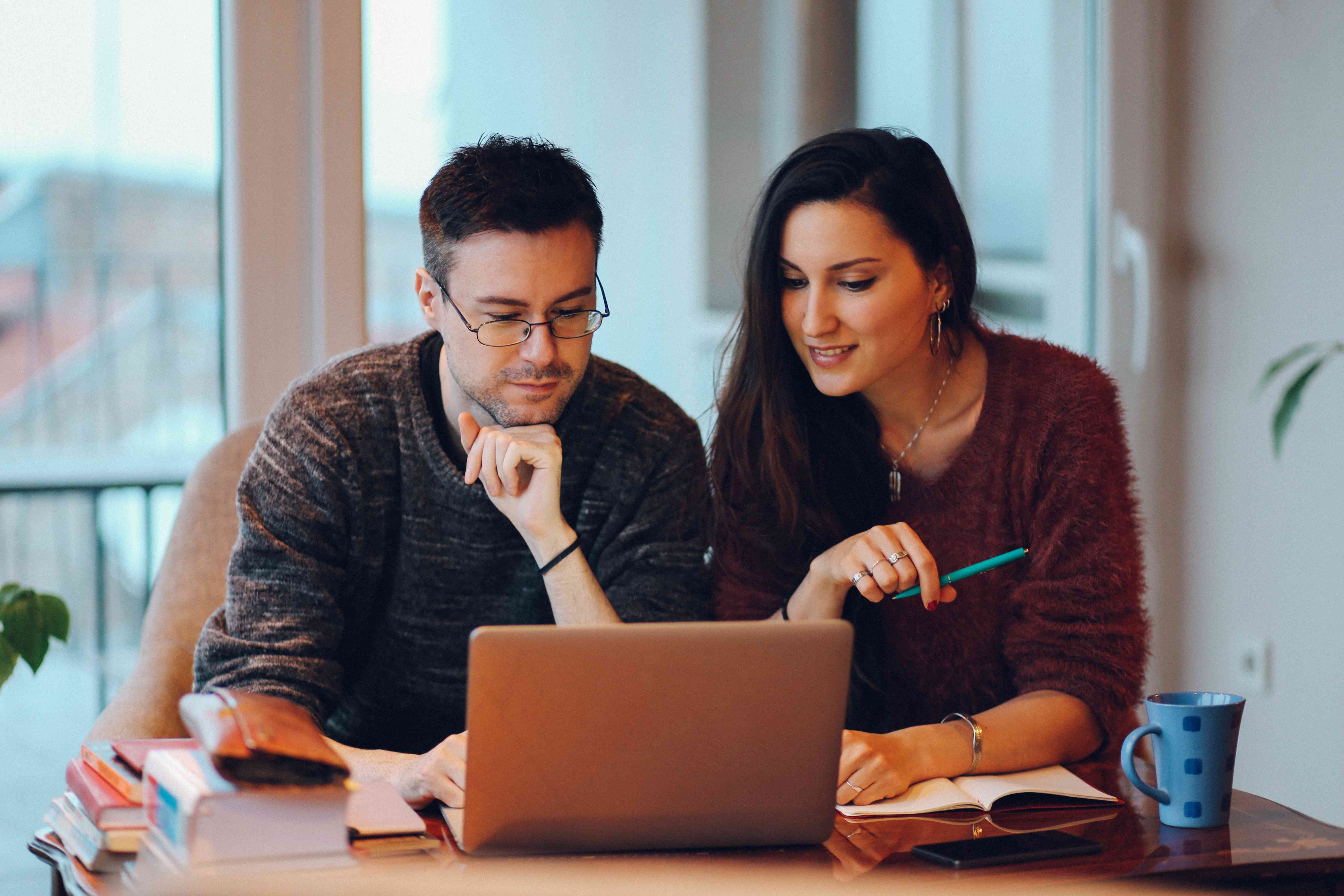 Young couple at home, looking together at a laptop screen and faintly smiling