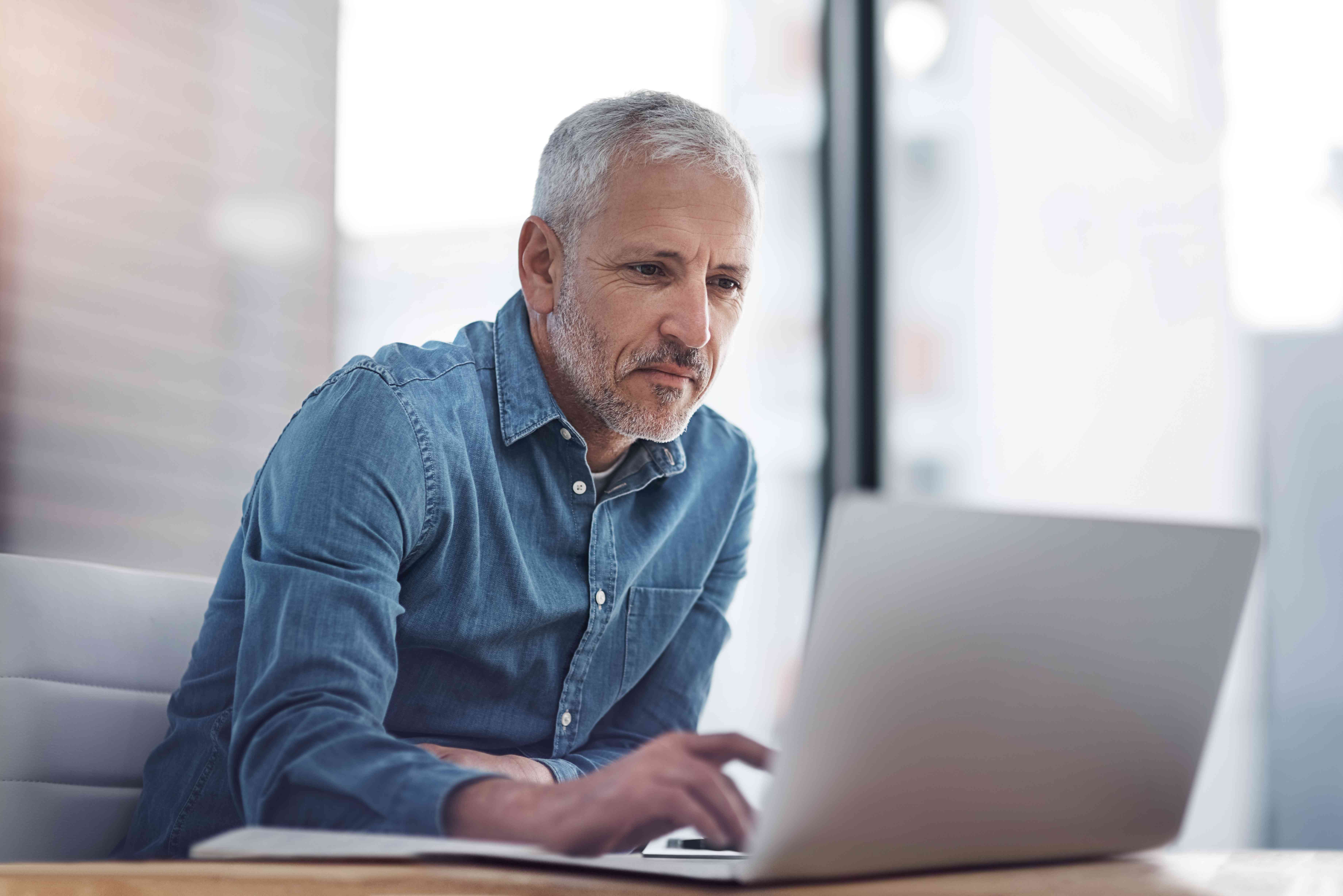 Older man in casual clothes at a work desk and looking intently at a laptop screen