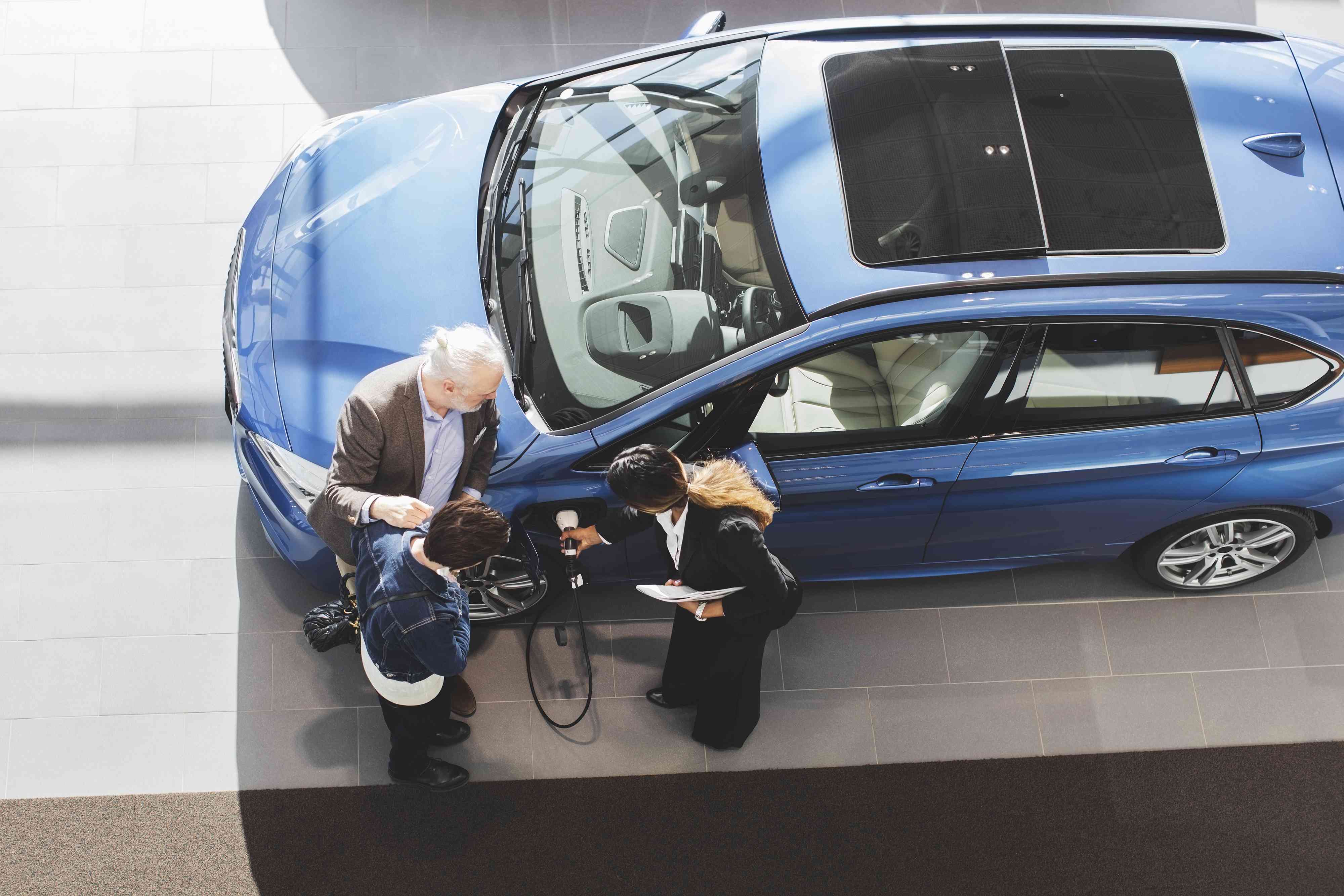 Saleswoman explaining customers to charge electric car at showroom