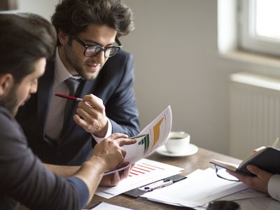 Business people analyzing documents around a table and drinking coffee.