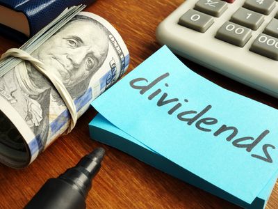 A roll or money laying next to a sticky note with the word dividends.