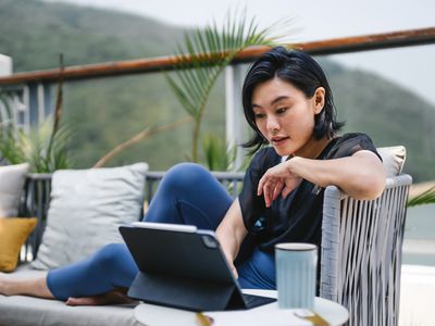 Young Asian woman sitting on the balcony, looking at her finances on a tablet computer.