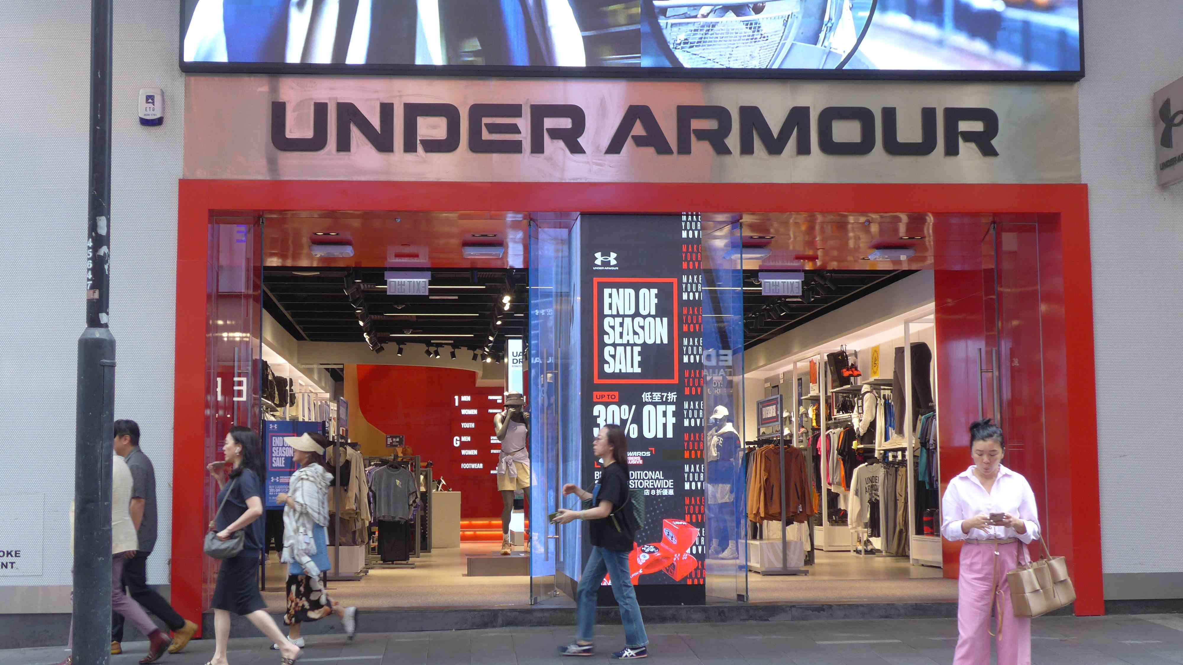 Pedestrians walk past the American sportswear company Under Armour logo and store in Hong Kong