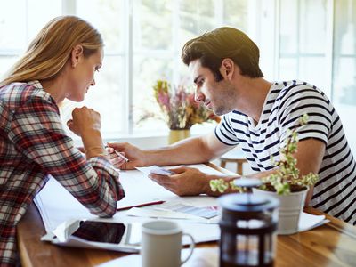 A young woman and a young man review documents together in a brightly light kitchen.