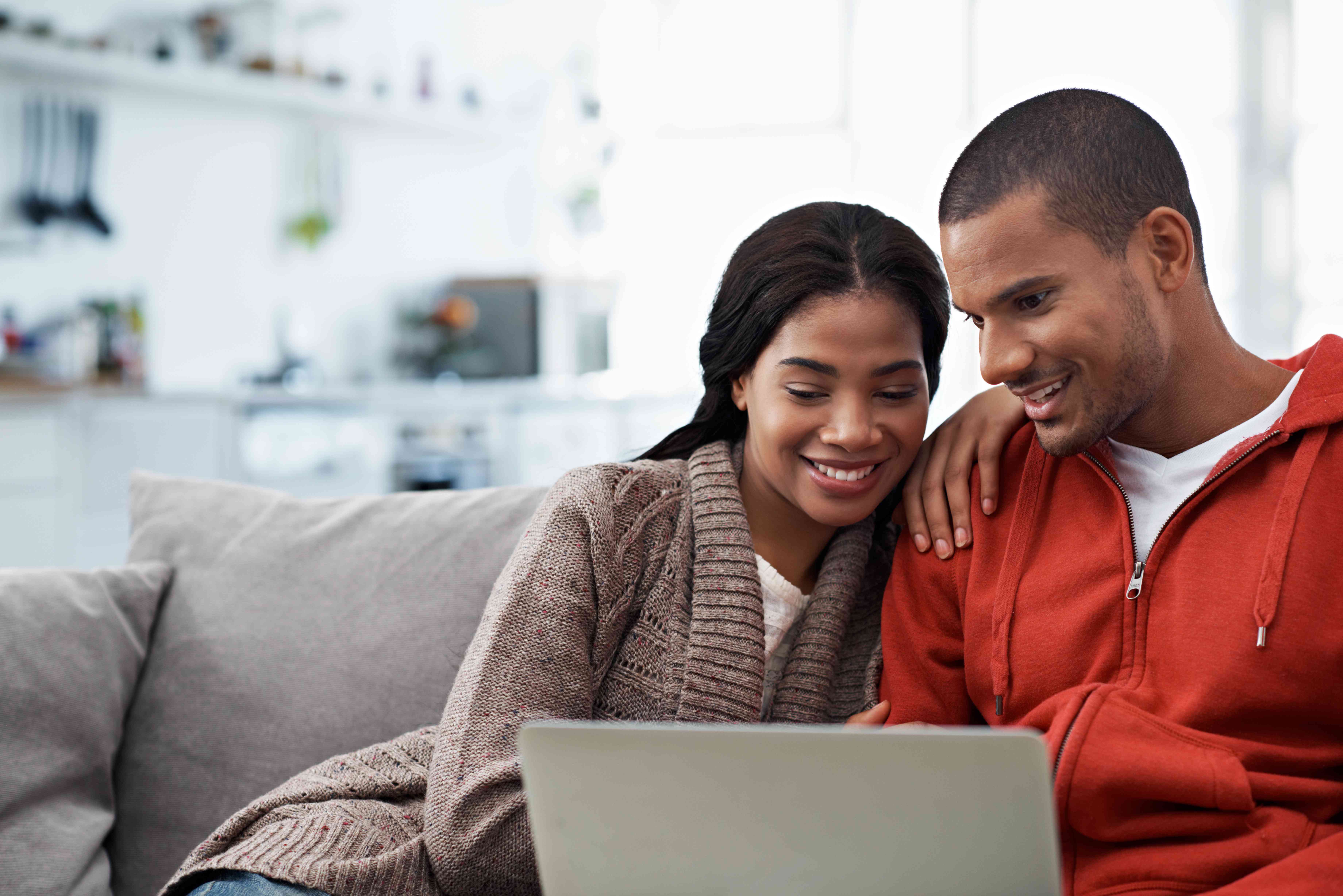 Young couple sitting on living room couch and looking happily together at a laptop screen