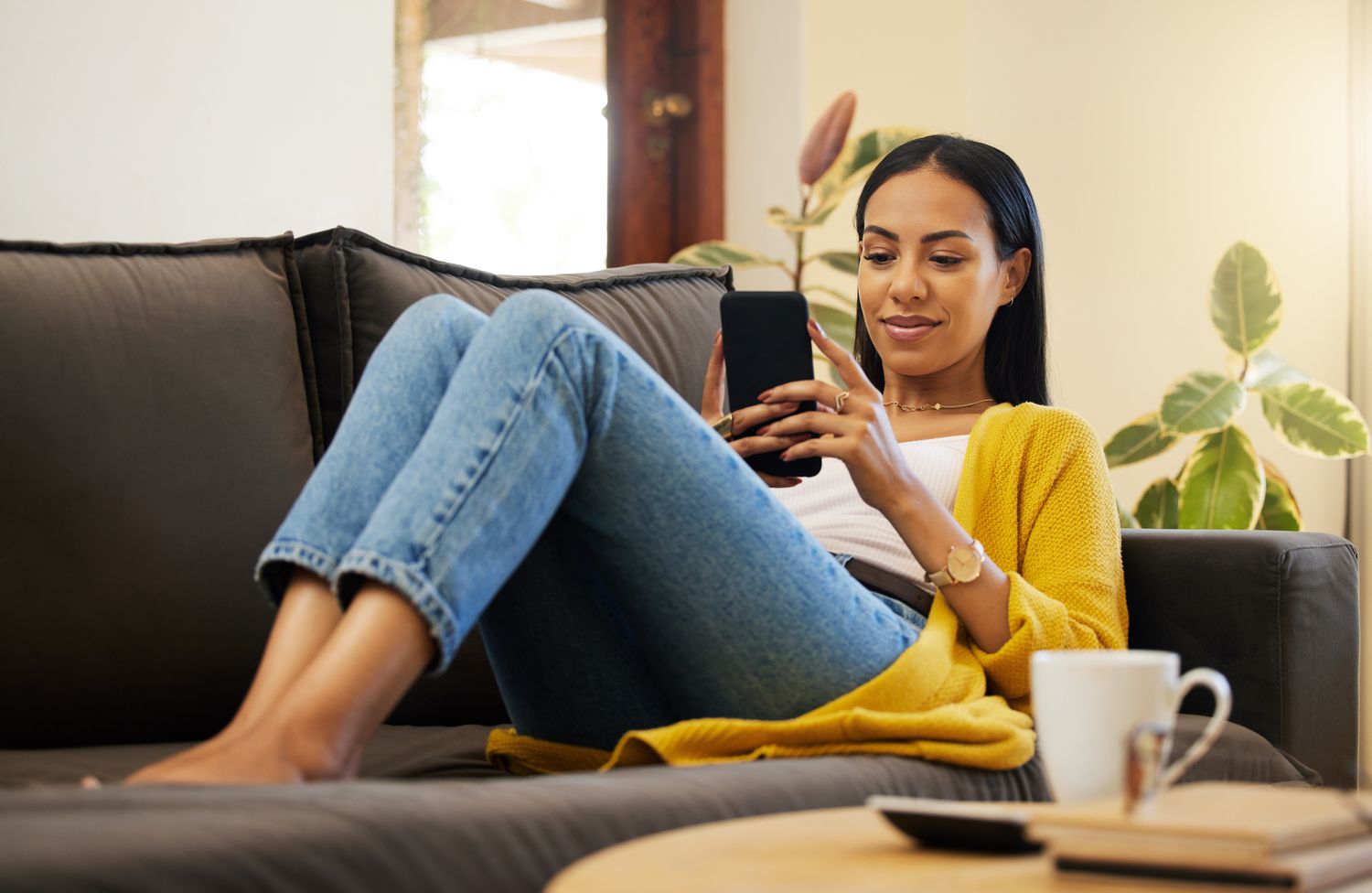 Woman in her late 20s to early 30s relaxing on her couch while she looks at her smartphone with a slight smile