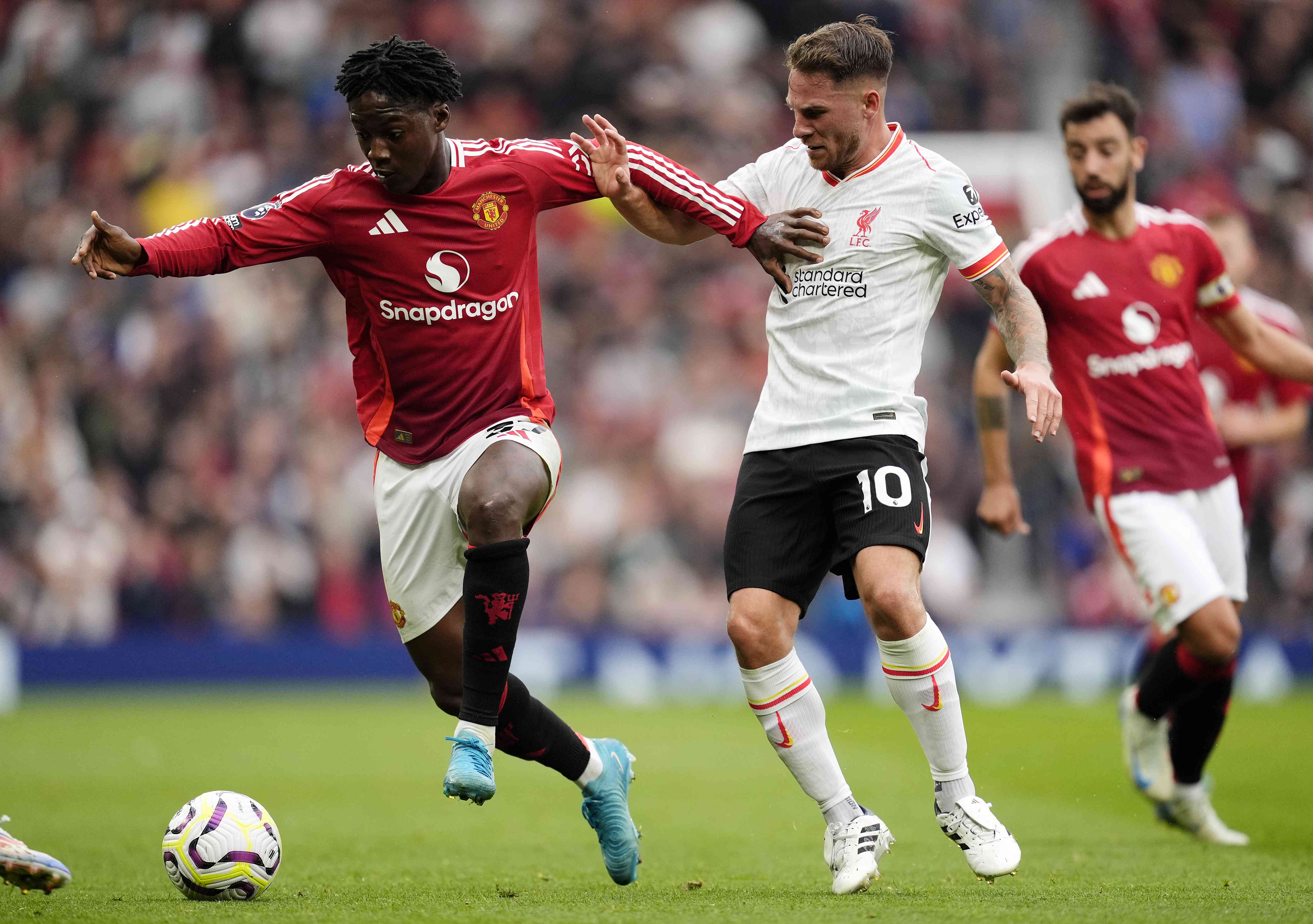 A Manchester United player dribbles a soccer ball away from a Liverpool player.