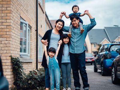 Cheerful Young Family Standing In Front Of House