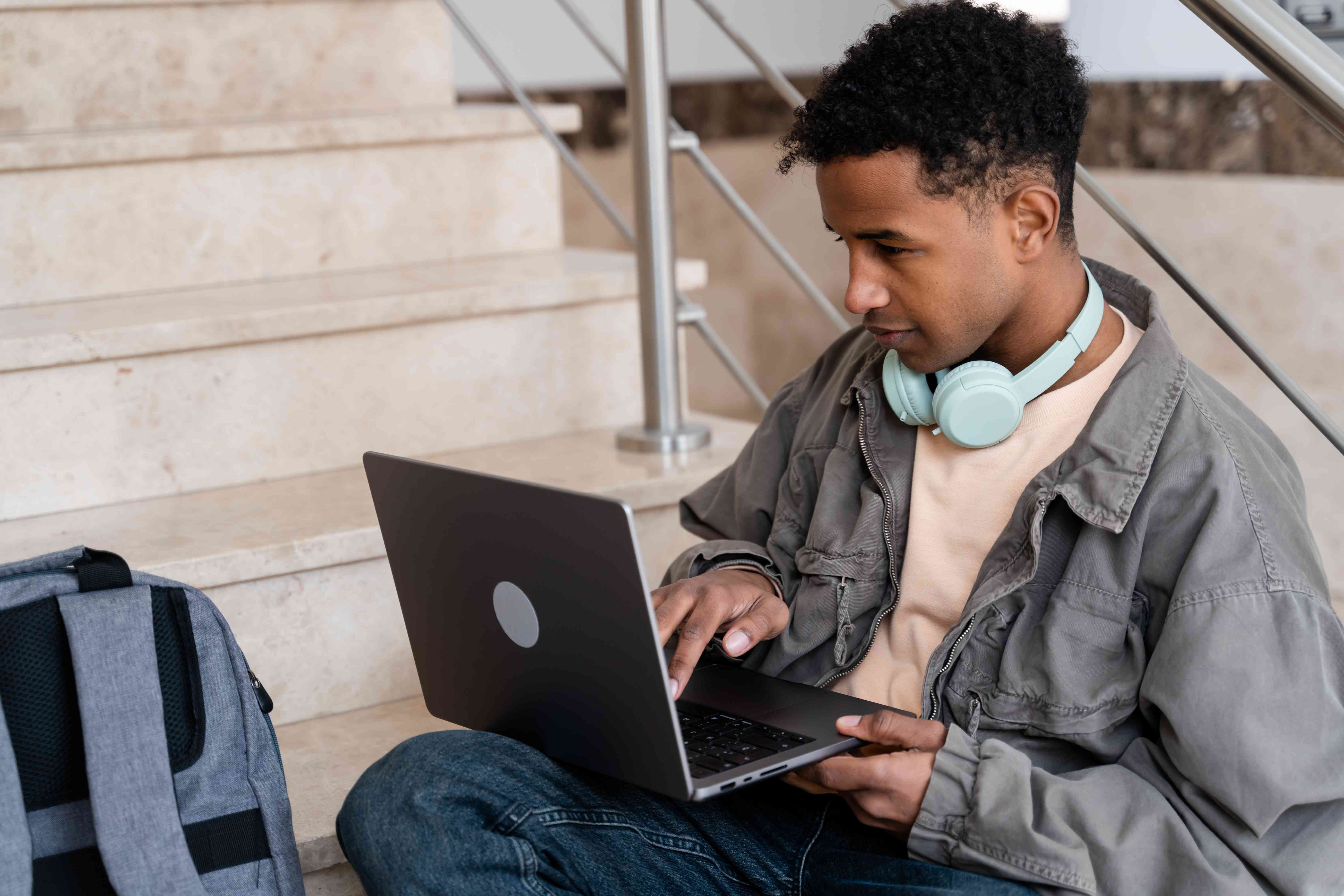 A student studies what discretionary income on their student loans is on the laptop while sitting on the stairs.