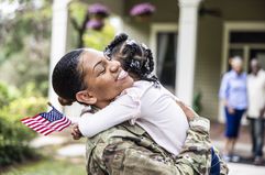 Daughter embracing U.S. soldier mother in front of their home.