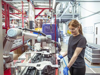 Female worker working with cobot, a collaborative robot, in robotic assembly machine in automotive parts factory