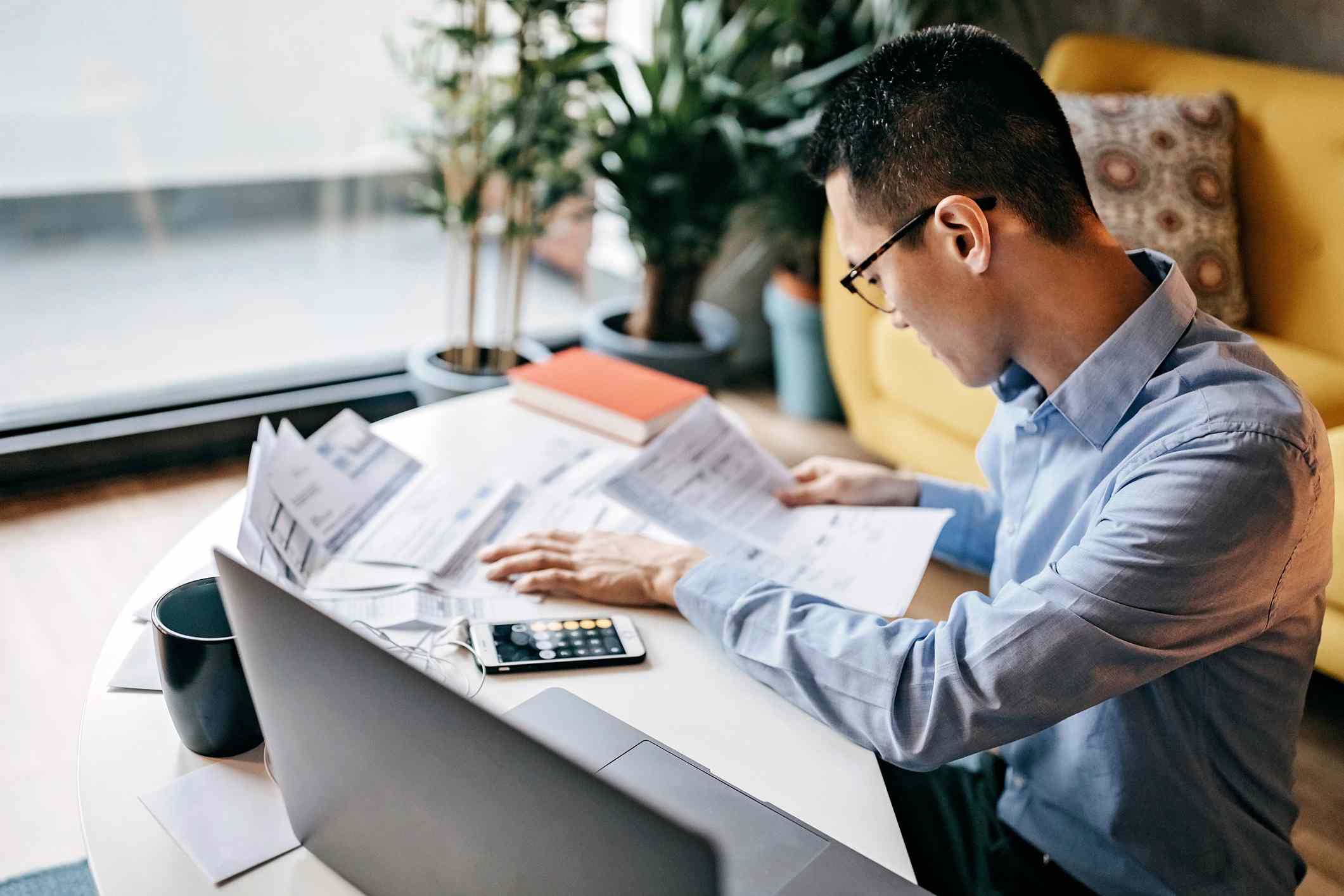 a man looking at papers on his desk in front of a laptop