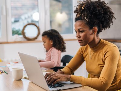 Young mom sitting at the family's kitchen table, doing some research on her laptop