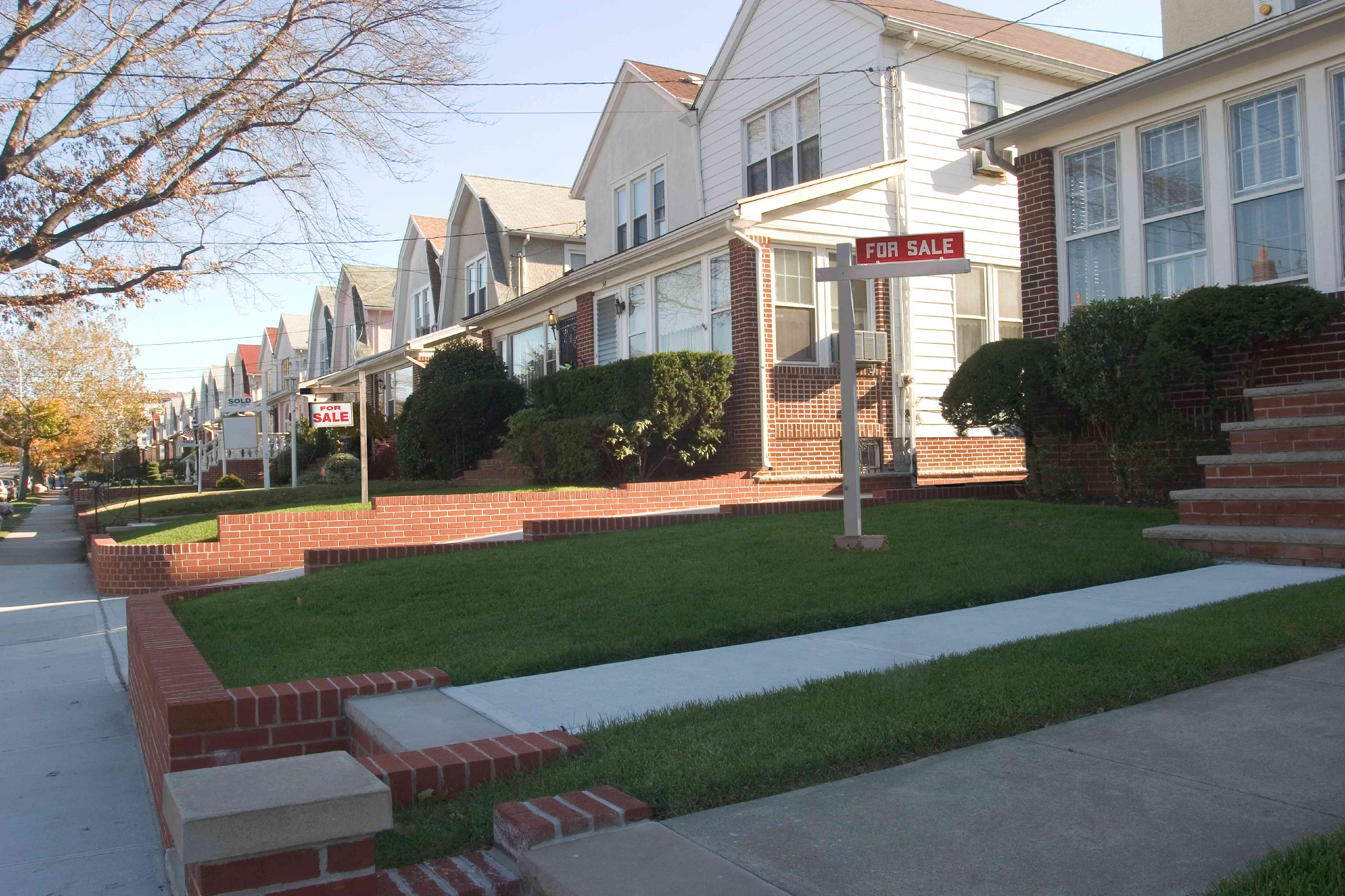 A row of suburbian homes with "For Sale" signs in the front yard.