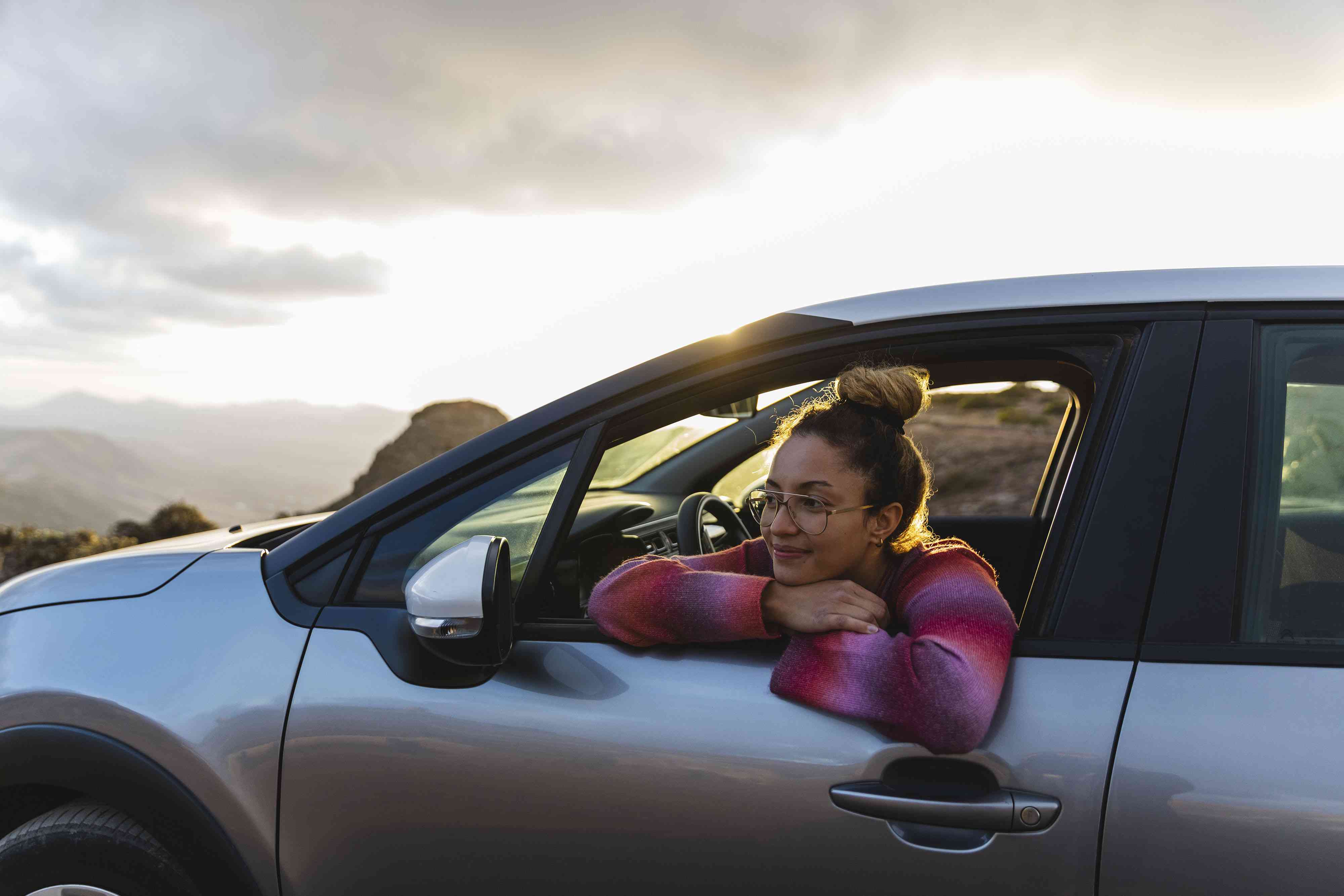 Smiling woman leaning out of car window at sunset