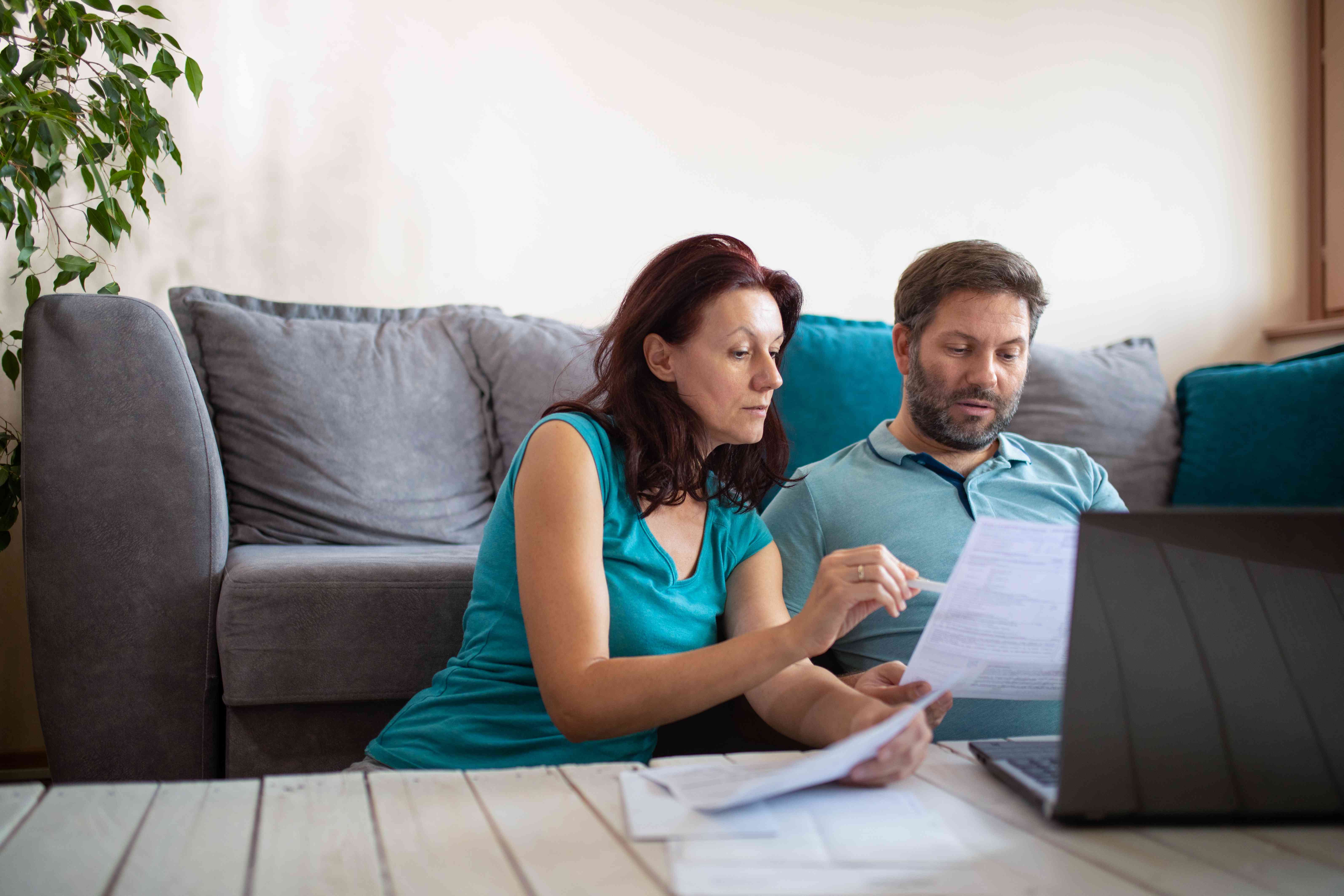 couple looking at paper and laptop while sitting on the floor in front of their couch