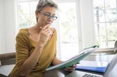 Woman at a laptop holding a folder in a home office 