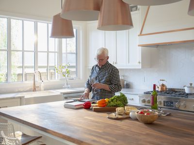 Senior Man Cooking, Drinking Wine, and Looking at Cookbook in Kitchen