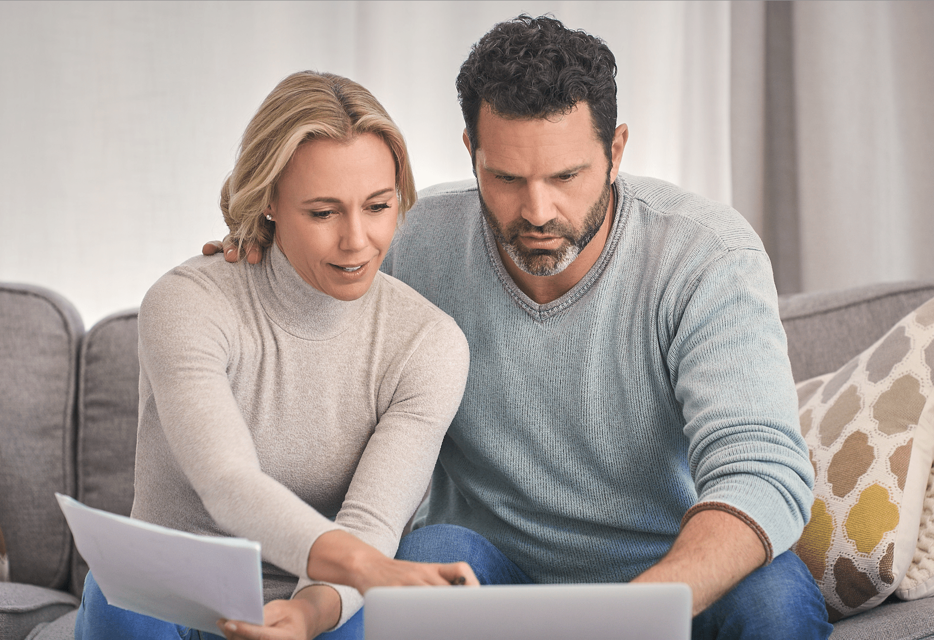 Couple in their 40s on their living room couch and looking together at a laptop and documents