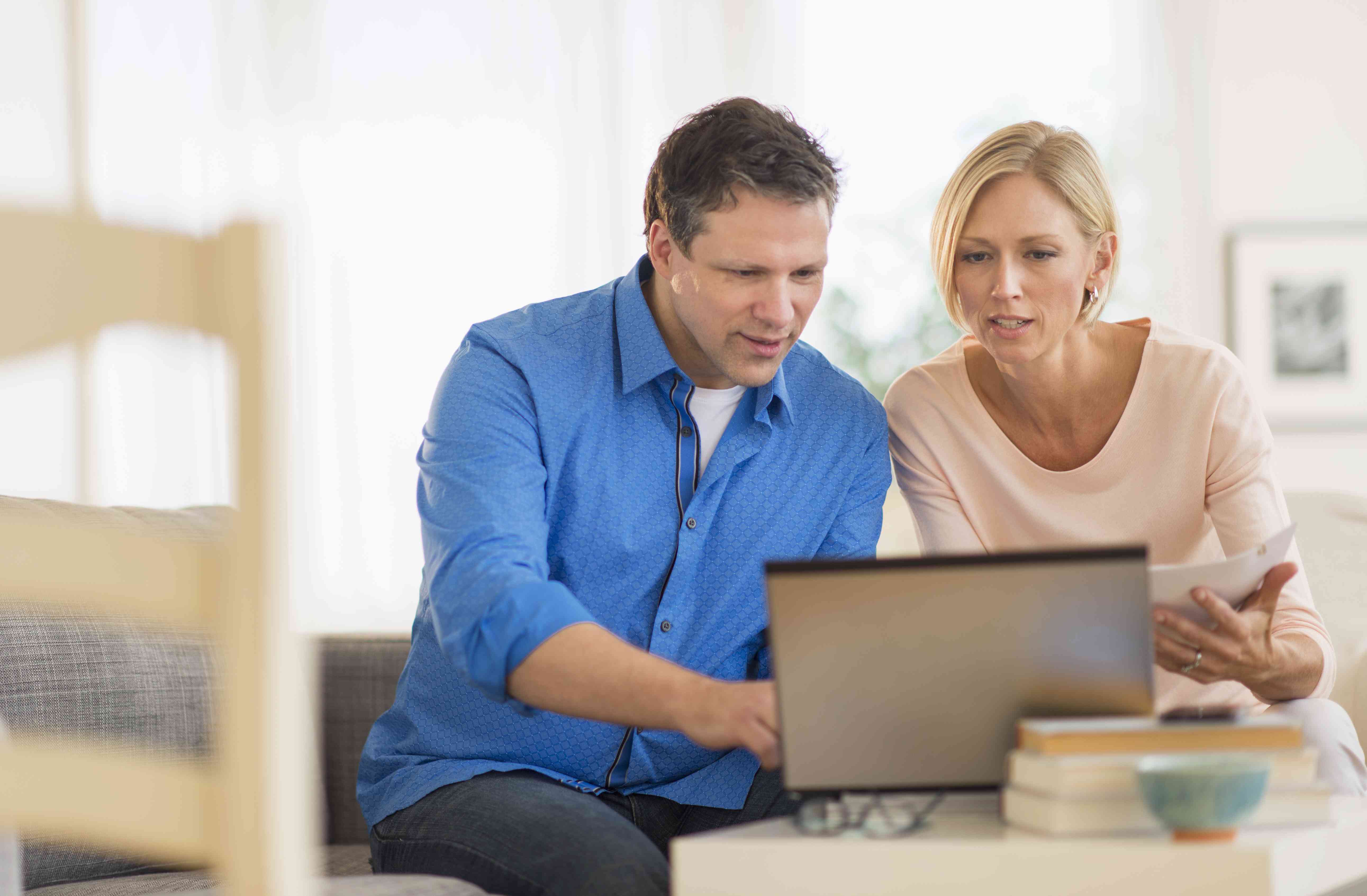 Couple in their 30s or 40s at home, looking together at a laptop screen and financial documents