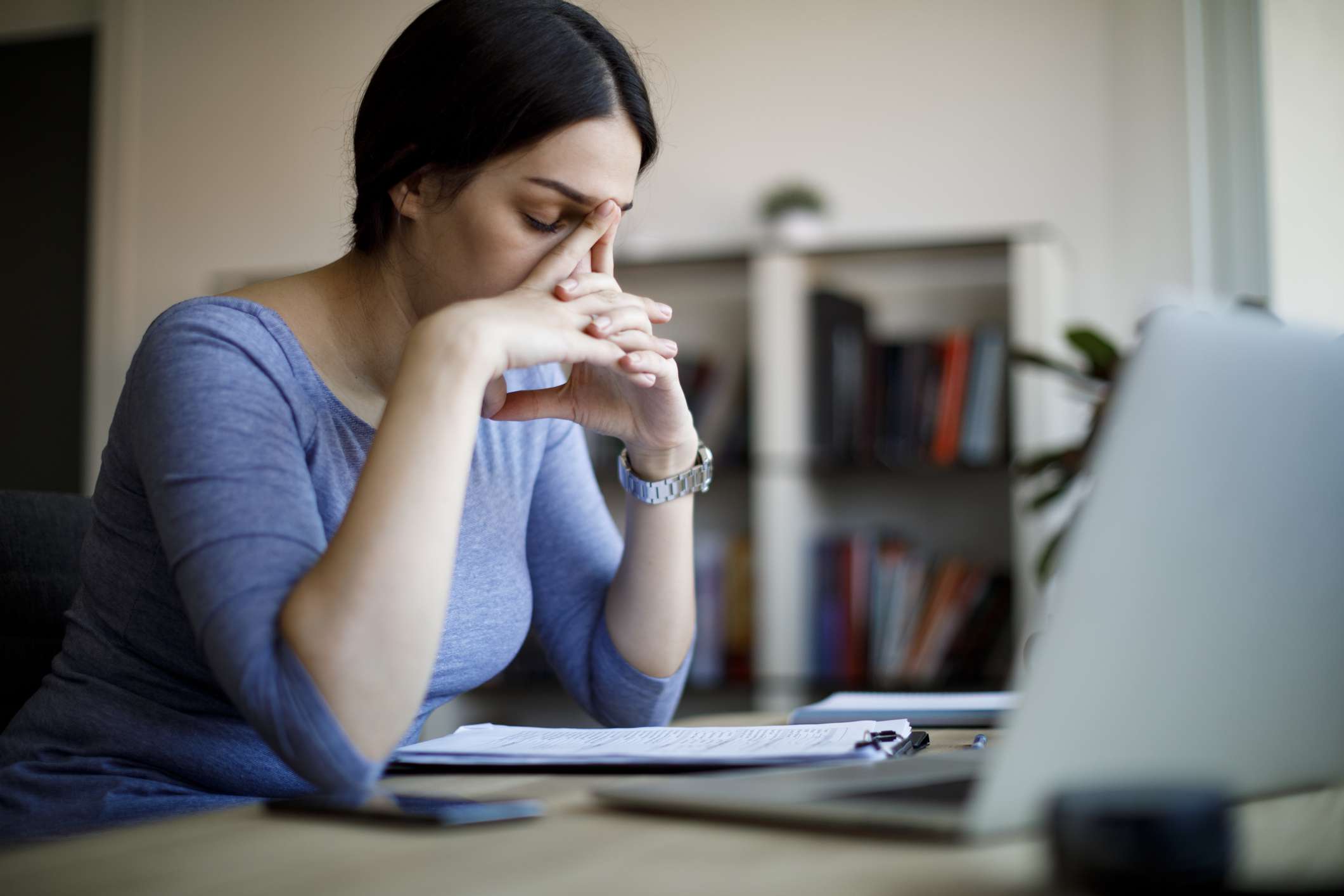 Person in blue shirt with hands on their face in front of a computer