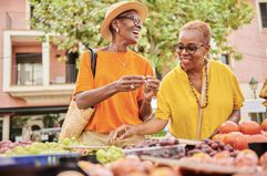 Two mature women shopping at an outdoor food market. 