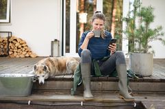 Homeowner drinking coffee on the front porch next to a dog while reading the defeasance clause included in mortgage contract on the phone.