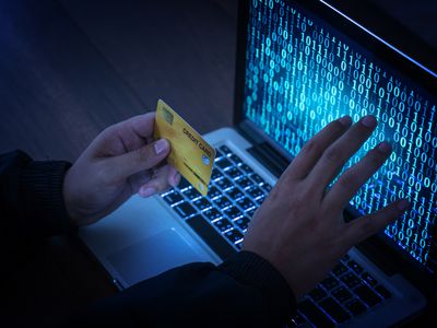 Hands of anonymous hacker holding credit card in front of a laptop