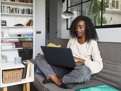 A woman sits on a couch with her legs crossed looking at a laptop