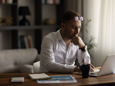 Man in his 30s at his home desk, looking intently at a laptop