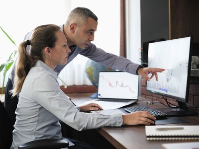 A man and a woman in an office setting looking at a stock chart utilizing stock strategies. 