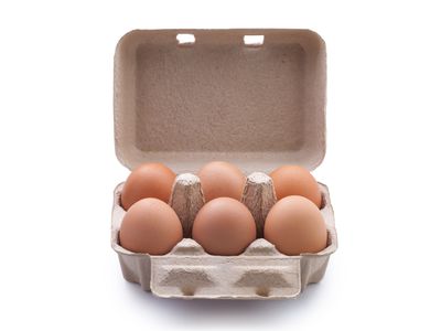 Close-Up Of Brown Eggs In Carton Over White Background